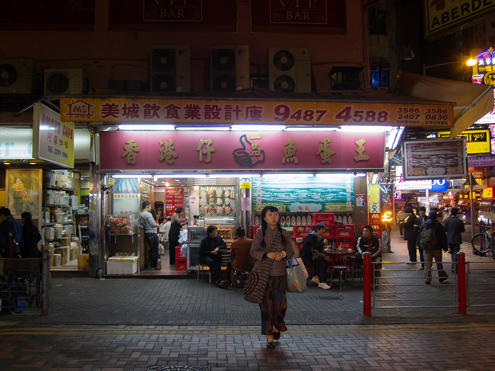Night Photo of Hong Kong Street with Young Woman Walking Towwards the Camera.